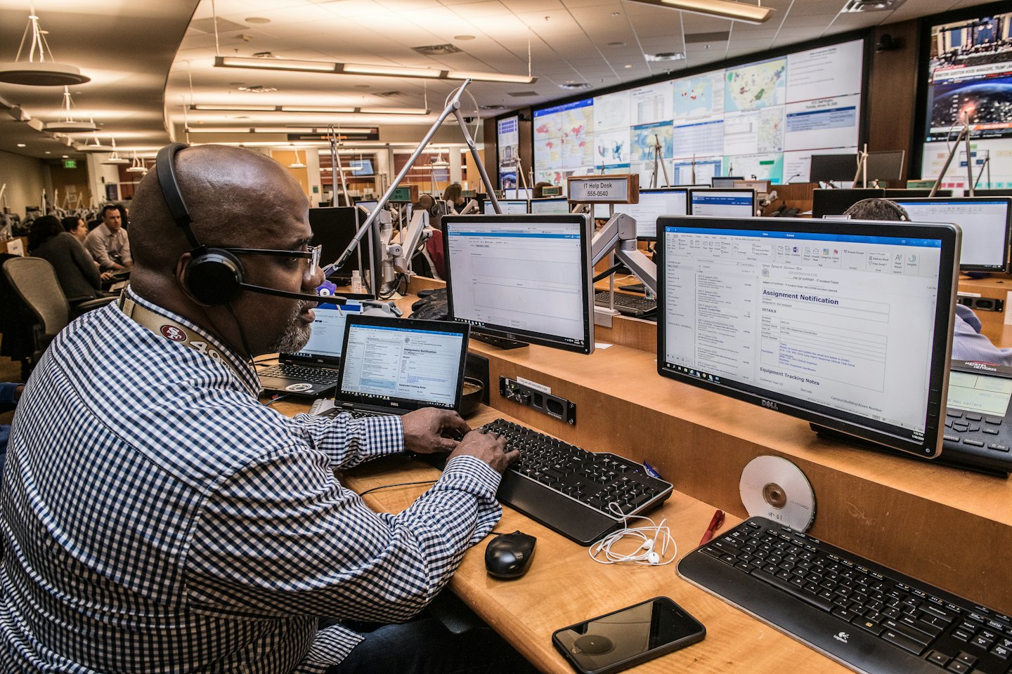 Man wearing a headset types on a computer keyboard surrounded by screens.