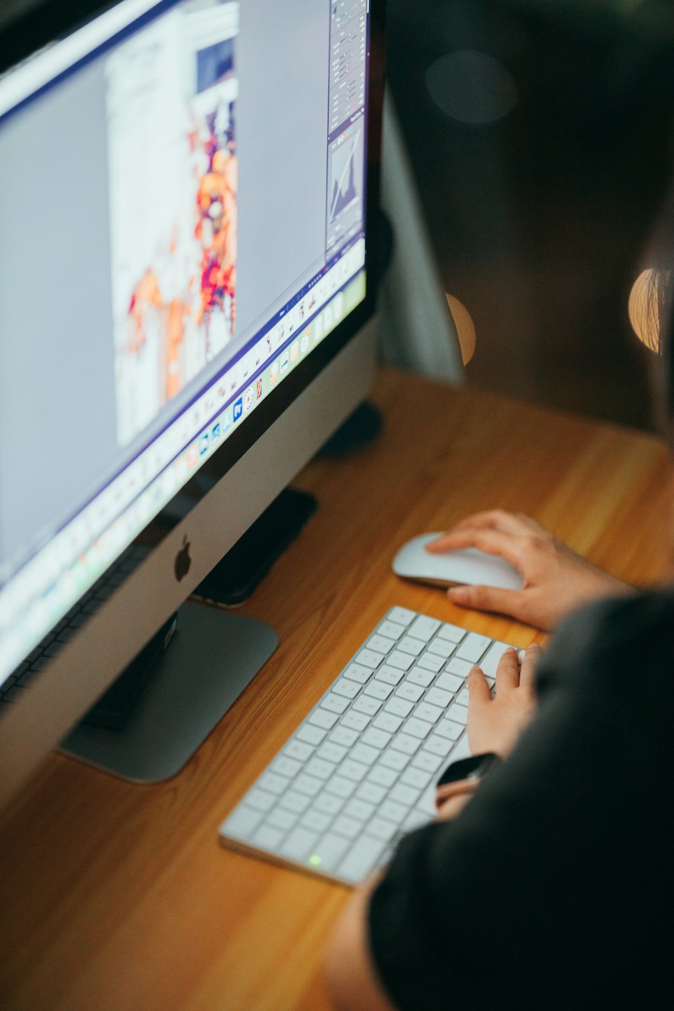 Hands typing on a keyboard in front of a colorful monitor.